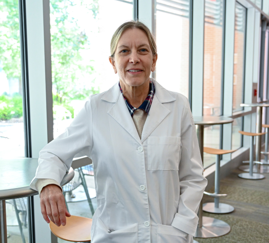 Standing women poses with one arm resting a table in her dental white coat.