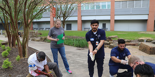 A group of students provide emergency care to a man laying on the ground in the park  with a mock wound. (Photo by UTHealth Houston)