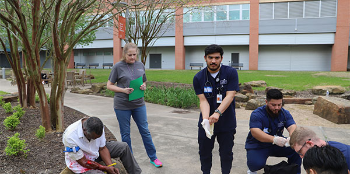 A group of students provide emergency care to a man laying on the ground in the park  with a mock wound. (Photo by UTHealth Houston)